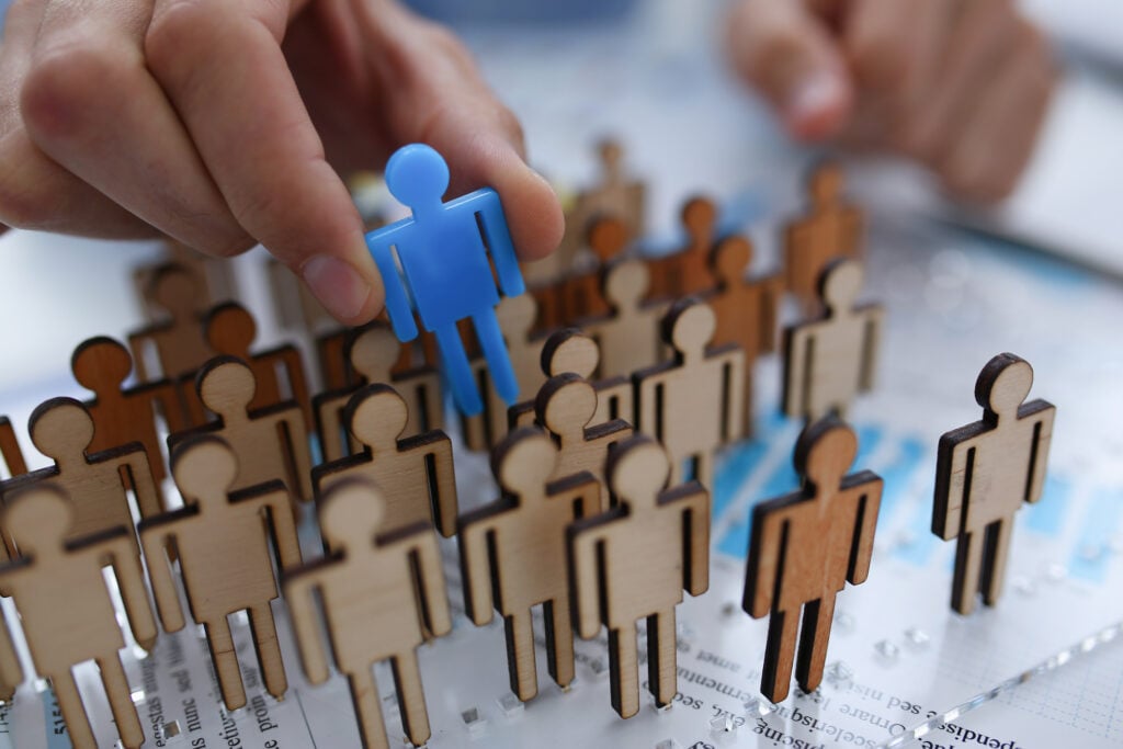 A hand selecting one individual from a crowd, symbolizing how attackers only need to compromise a single employee to breach an organization.